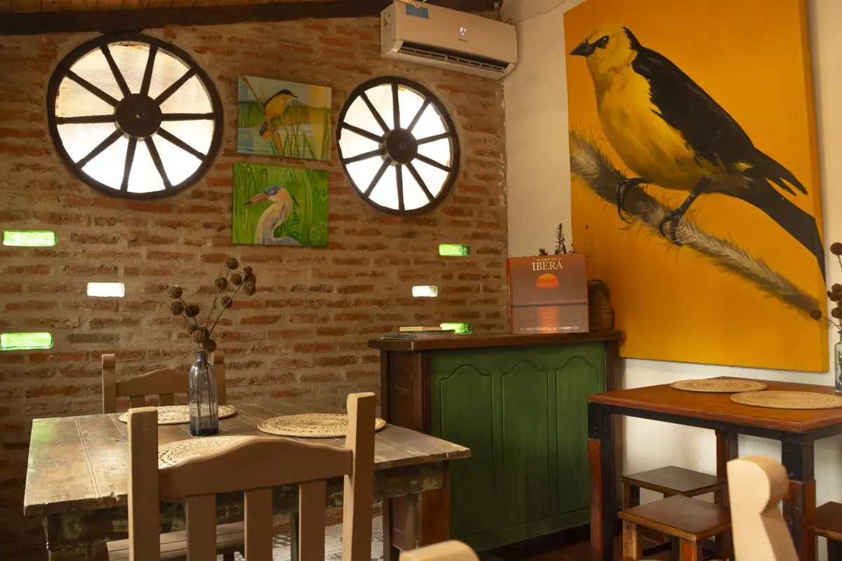 Comedor con paredes de ladrillo, cuadros de aves y mesa de madera