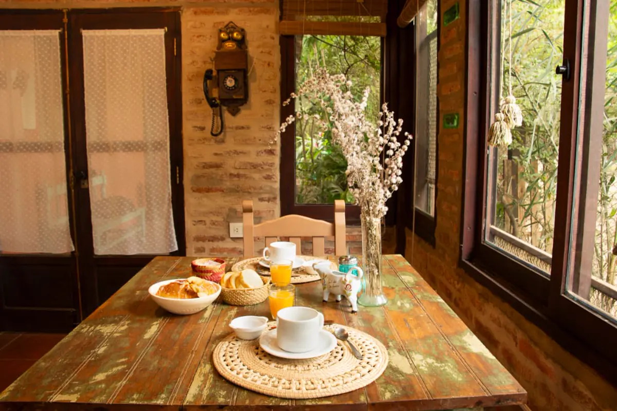 Mesa de desayuno junto a la ventana, con jugo, medialunas y flores