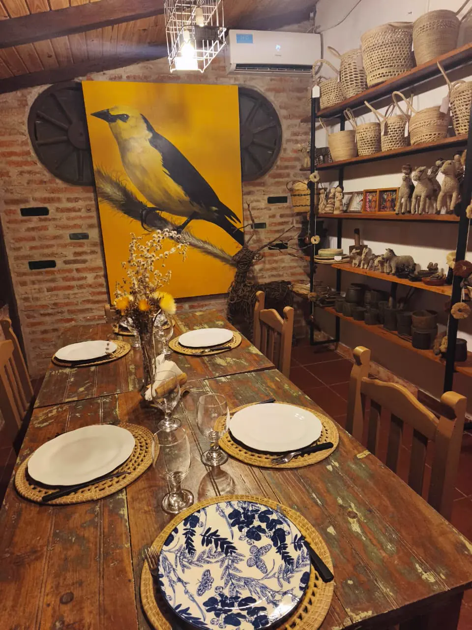Mesa servida frente a un cuadro de ave y estantes con artesanías
